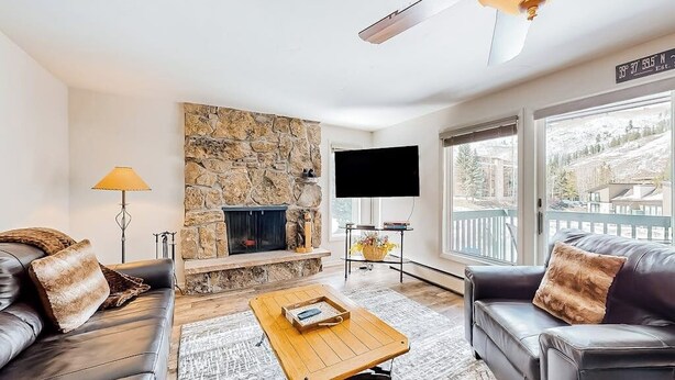 A living room with a stone fireplace, leather sofas, a coffee table, and a large window with a view. - Mountain view condo with 2 balconies, pool & pickleball - steps to free shuttle (Vail)