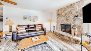 A living room with a stone fireplace, a leather sofa, a coffee table, and two floor lamps. - Mountain view condo with 2 balconies, pool & pickleball - steps to free shuttle (Vail)