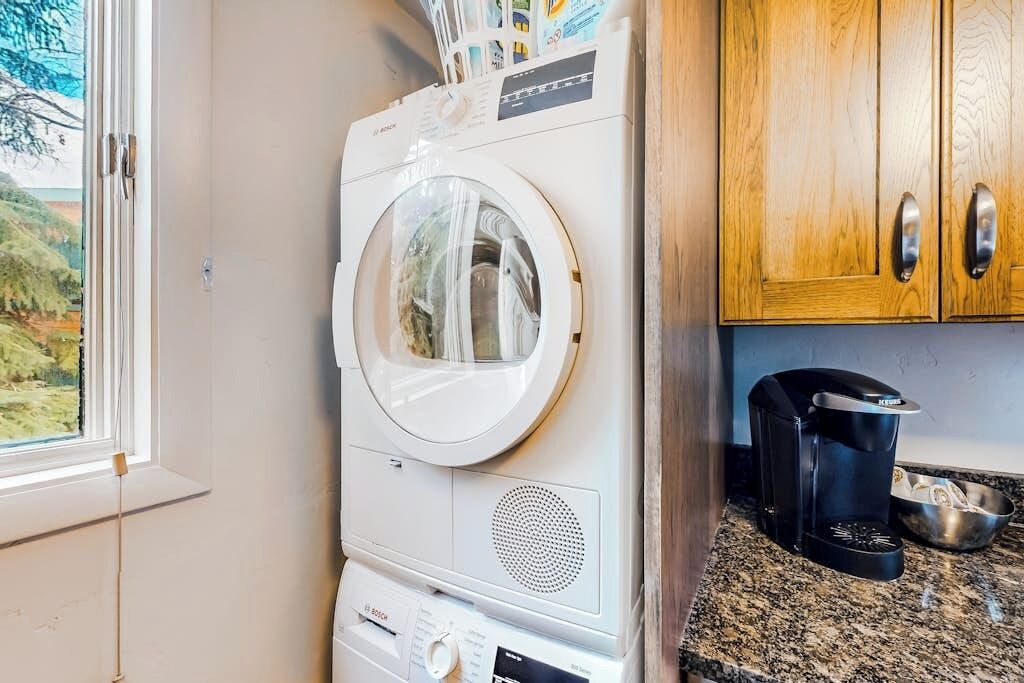 A compact washer and dryer unit in a kitchen area with wooden cabinets and a coffee maker on the counter.