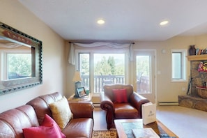 A living room with leather sofas, a fireplace, and a view of the outdoors. - Charming townhouse with private hot tub, mountain views, and family-friendly (Vail)