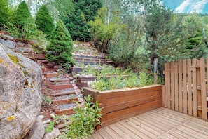 A wooden deck with a wooden fence, a stone wall, and a variety of plants. - Charming townhouse with private hot tub, mountain views, and family-friendly (Vail)