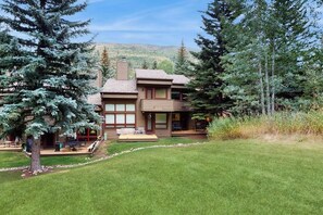 A two-story house with a covered patio, surrounded by trees and a grassy yard. - Comfortable home with fully stocked kitchen & W/D - great location (Vail)