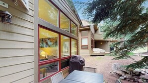 Un esterno in legno con ampie finestre, un tavolo da patio e una zona barbecue coperta.