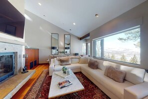 Ein modernes Wohnzimmer mit Kamin, großen Fenstern, einer Couch und einem Couchtisch.