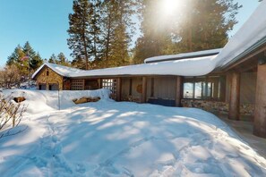Eine Holzhütte mit schneebedecktem Dach, umgeben von Bäumen und einem klaren Himmel.