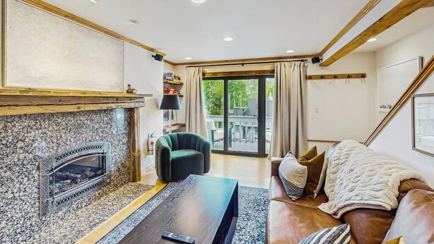 Una sala de estar con chimenea, sofá, mesa de centro y vistas al exterior a través de un ventanal.