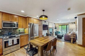 A modern kitchen with wooden cabinets, stainless steel appliances, and a dining area with a wooden table and chairs. - Conveniently located condo w/ full kitchen, W/D & balcony with great views (Vail)
