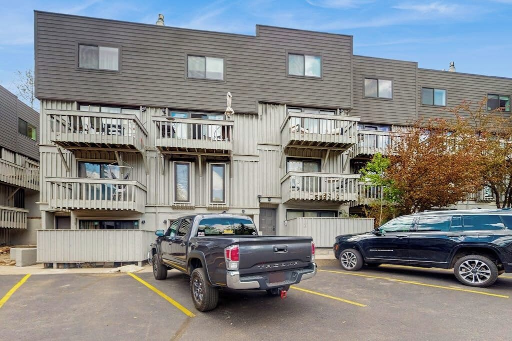 Un immeuble à plusieurs étages doté de balcons, d’un parking et de deux véhicules stationnés.
