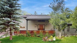 A house with a front porch, a small garden, and a tree in the foreground. - Luxurious Vail Home with private hot tub, patio, fireplace, and bus to slope (Vail)