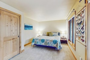 Ein Schlafzimmer mit Bett, Nachttischen, Wandbild mit Schmetterlingen, einer Holztür und einem Fenster.
