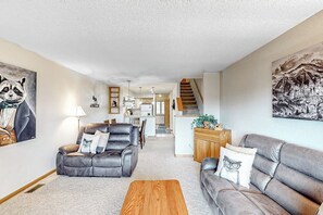 Ein geräumiges Wohnzimmer mit Sofa, Sesseln und Couchtisch. Eine Treppe führt auf eine obere Ebene.