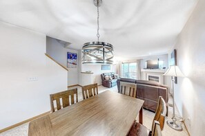 Ein Essbereich mit Holztisch und -stühlen, einer modernen Kronleuchter, einer Couch und einem Fernseher im Hintergrund.