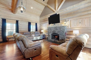 Ein Holzblockhaus-Interieur mit Kamin aus Stein, Ledersofas und einem flachbildfernseher, der darüber angebracht ist.