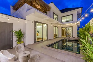 Ein modernes Haus mit Pool, Sitzgelegenheiten im Freien und Lichterketten.