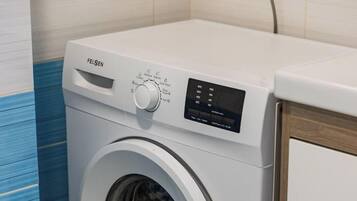 Lavadora de carga frontal con panel de control, ubicada en una habitación con piso de baldosas y pared de acento azul.
