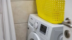 A front-loading washing machine with a yellow basket on top, a white door, and a tiled floor. - Adriatic Escape Apartment Steps From the Beach (Shengjin)