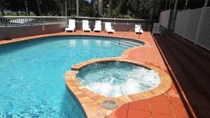 En swimmingpool med ett bubbelbad, omgiven av vita solstolar och en kakelbeklädd terrass.