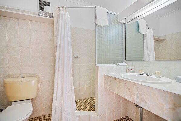 Un baño con inodoro, ducha, lavamanos y espejo.