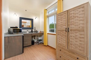 Eine kleine Küche mit Mikrowelle, Spüle und Schränken, ein Fenster mit gelben Vorhängen sowie ein Holzschrank.