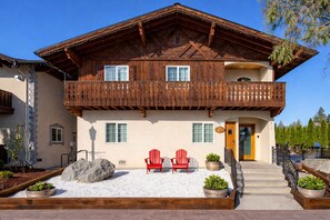 Eine zweistöckige Holzchalet mit Balkon, Steinstufen und Sitzgelegenheiten im Freien.