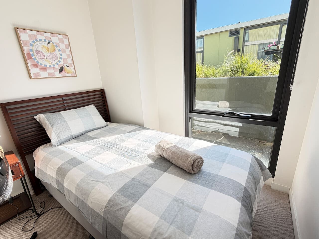 A bedroom with a bed, a bedside table, a window, and a view of greenery outside.
