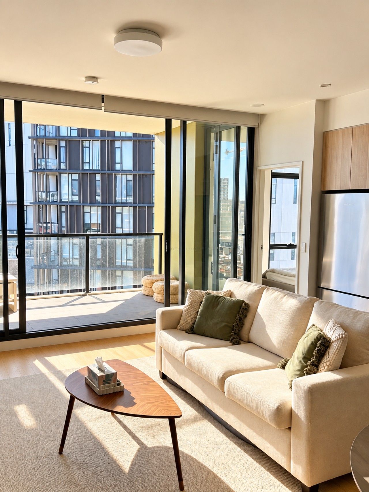 A modern living room with a sofa, a coffee table, and a view of a cityscape through large windows.