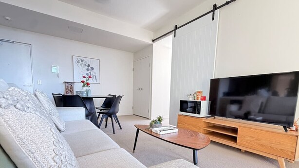 Una sala de estar moderna con un sofá, una mesa de centro, un televisor y una zona de comedor con sillas.