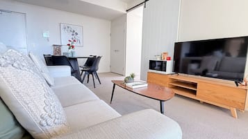 A modern living room with a sofa, a coffee table, a TV, and a dining area with chairs.