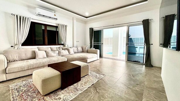 Ein modernes Wohnzimmer mit einer Couch, einem Couchtisch, einem Teppich und einem großen Fenster mit Vorhängen.