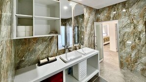 Ein Badezimmer mit Marmorwänden, einem weißen Waschtisch mit Spiegel und einer Duschkabine.