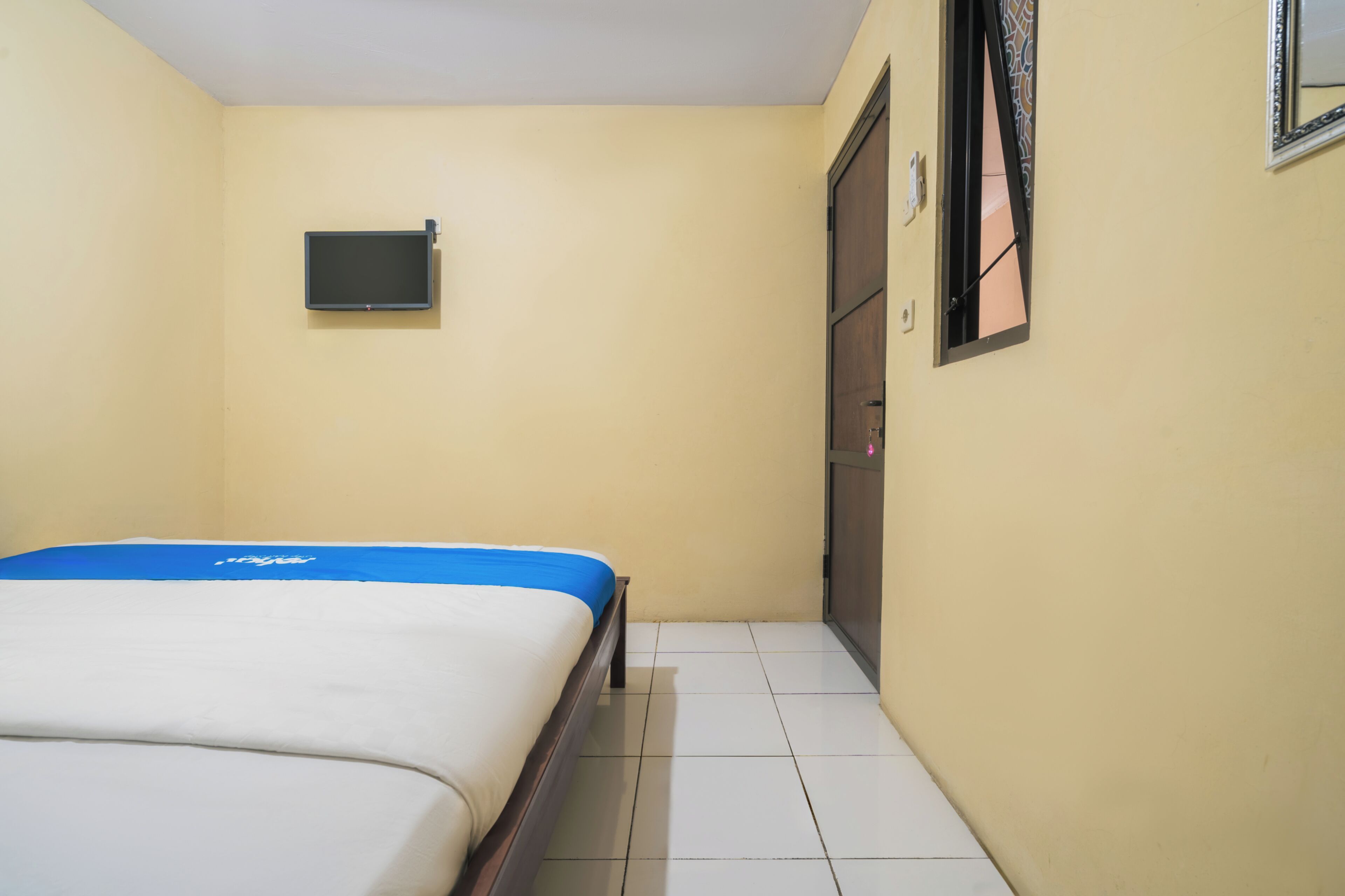 A room with a bed, a television mounted on the wall, a door, and a window with a view.