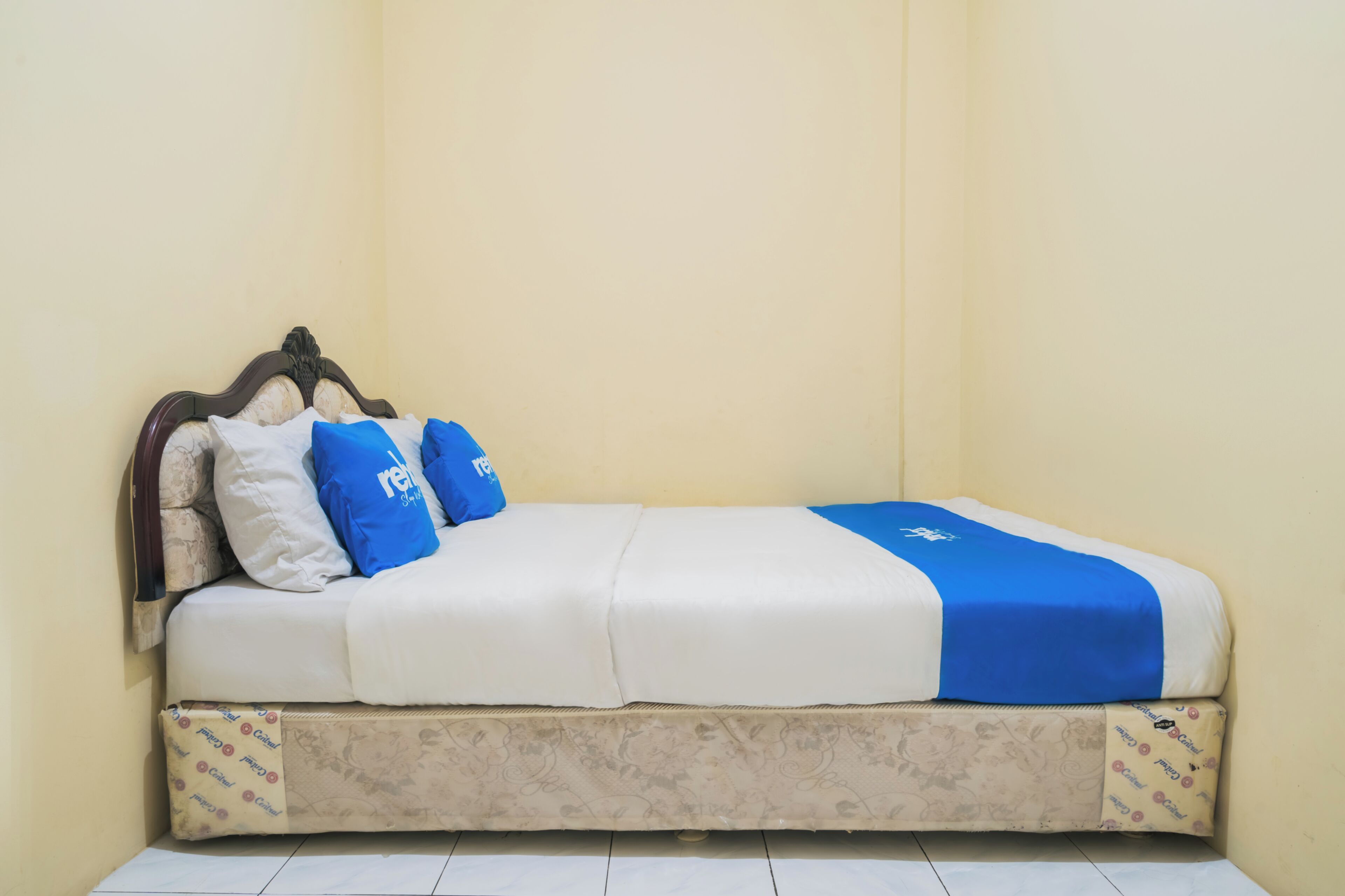 Una cama individual con cabecera, ropa de cama blanca y azul, y un cubrecolchón estampado.
