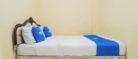 Una cama individual con cabecera, ropa de cama blanca y azul, y un cubrecolchón estampado.
