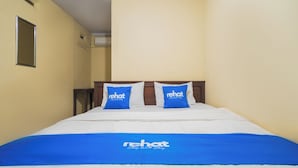 Habitación de hotel con una cama, dos almohadas con el logotipo del hotel y una colcha azul.