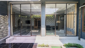 Un edificio moderno con amplias puertas de cristal, un patio empedrado y un pequeño jardín.