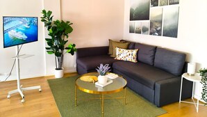 Ein modernes Wohnzimmer mit einer Couch, einem Couchtisch, einem Fernseher auf einem Schrank und einer Pflanze.