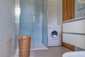 Un baño con cabina de ducha de vidrio, lavadora y cesta de mimbre.