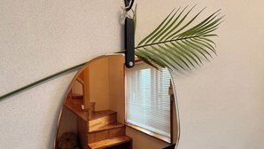 A mirror with a wooden staircase reflection, a plant, and a wall-mounted hook. - Spring Breeze Stay (Jeju City)