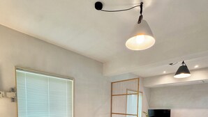 A modern bedroom with two beds, a large window with blinds, a TV, and a plant. - Spring Breeze Stay (Jeju City)