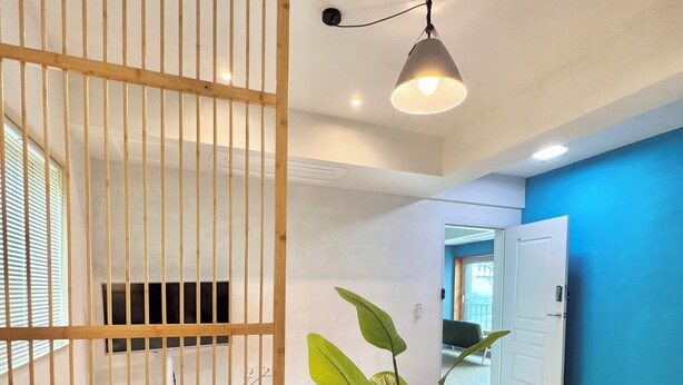 A room with a bed, a wooden partition, a potted plant, a hanging light fixture, and a blue wall. - Spring Breeze Stay (Jeju City)