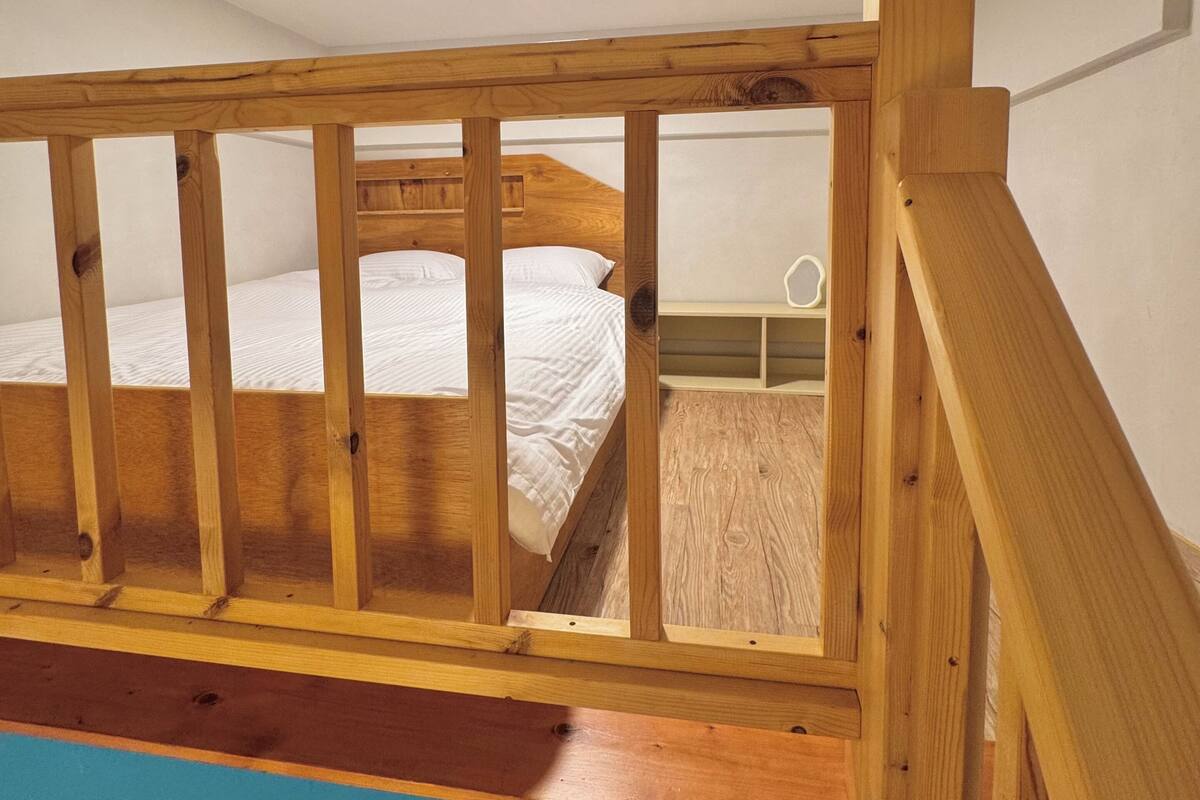 Un escalier en bois mène à une chambre où se trouvent un lit superposé et un lit simple.