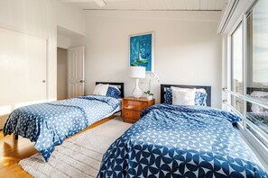Une chambre avec deux lits, une table de chevet, un tableau et une fenêtre.