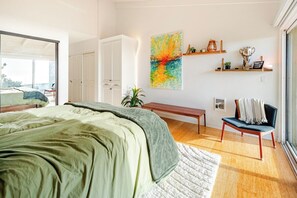 A bedroom with a bed, a bench, a chair, a large window, and a wall with shelves.