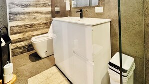 Ein Badezimmer mit Holzwand, Waschbecken in Weiß, Toilette und rotem Föhn.