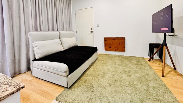 Ein Zimmer mit einem Bett, einem Schreibtisch, einem Sessel, einem Fernseher und einer Tür.