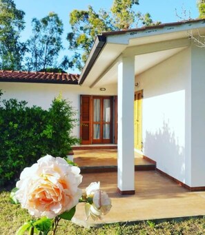 A house with a covered porch, a door with glass panels, and a garden with a rose. - Aria di Mare - Cottage (Capoliveri)