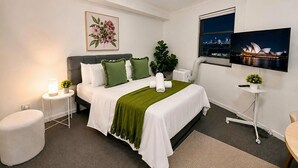 A modern hotel room with a bed, bedside table, lamp, and a television mounted on the wall. - Central Loft on Broadway + Parking/Pool (Glebe)