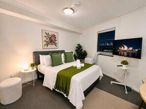 A modern hotel room with a bed, bedside table, lamp, and a television mounted on the wall. - Central Loft on Broadway + Parking/Pool (Glebe)