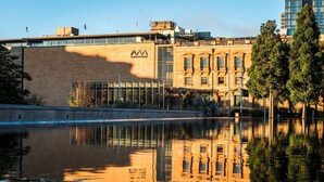 A building with a brick facade, a glass section, and a reflection in a body of water. - Central Loft on Broadway + Parking/Pool (Glebe)