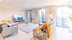 A modern living room with a sofa, armchair, TV, and a balcony with sliding doors. - Luxury Penthouse with Natural Light (Glebe)